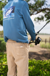 Person wearing a blue jacket with a fish design and text, holding a fishing rod outdoors. boy. boys. south. soutehrn. pants.