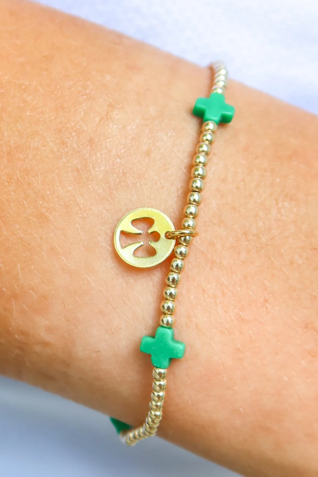 Gold bracelet with green charms on a wrist against a light background. Gold beaded bracelet on a white background. enewton. 14k gold, tarnish free. low price. camp mystic