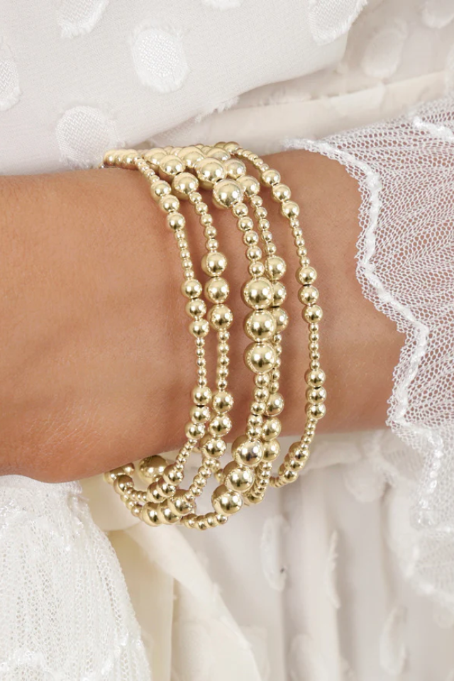 Gold beaded bracelets on a wrist with a white lace background. Gold beaded bracelet on a white background. enewton. 14k gold, tarnish free. low price. 