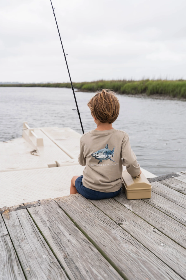 Child sitting on a dock fishing with a shirt featuring a shark design. shark, polo, tee. t-shirt. southern. boy. boys 